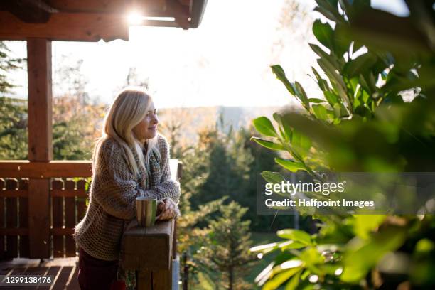 happy senior woman with tea outdoors on terrace in autumn, relaxing. - tranquility stock-fotos und bilder
