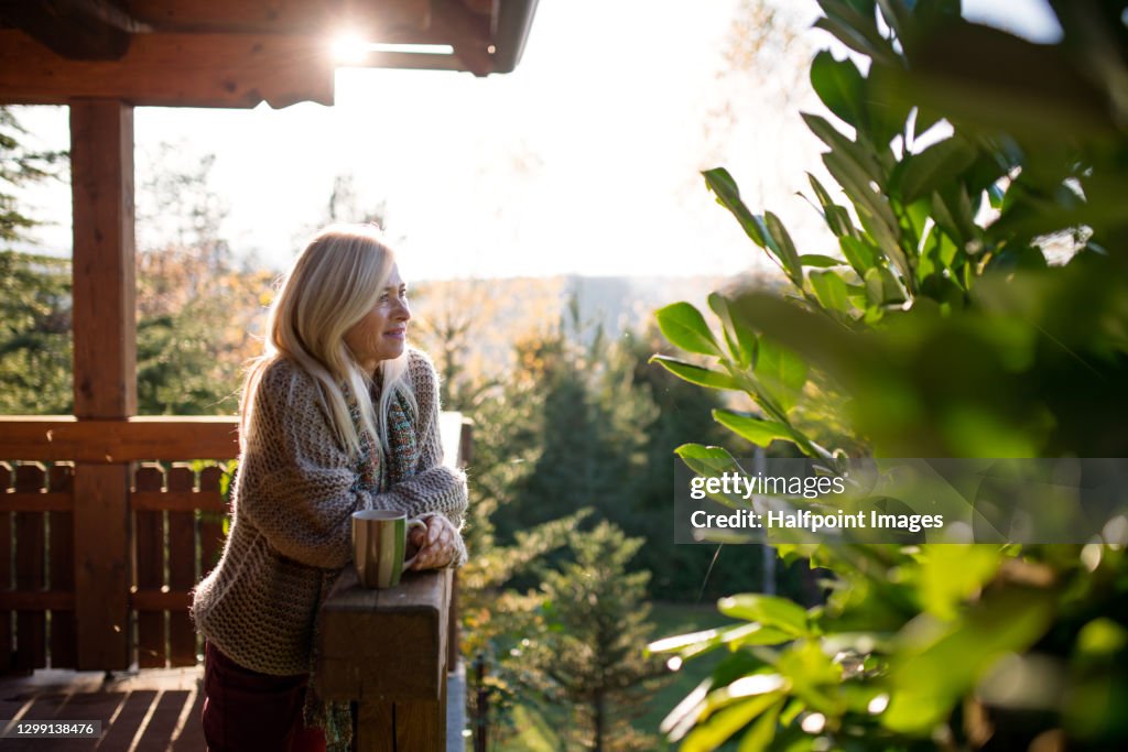 Happy senior woman with tea outdoors on terrace in autumn, relaxing.