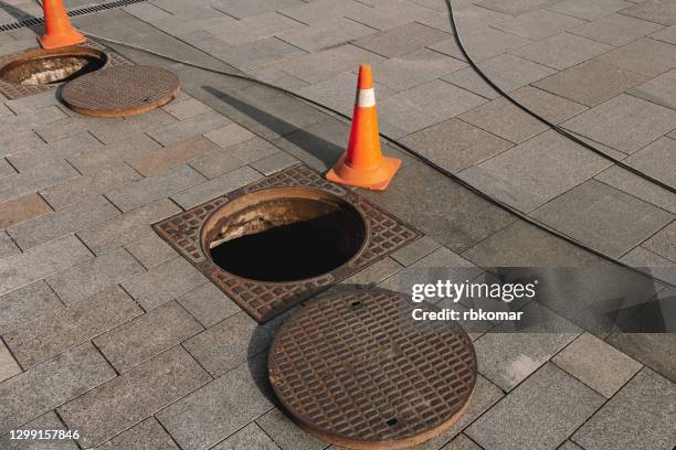 manhole cover open in street and repair of roads. accident with sewer hatch in city - égout photos et images de collection