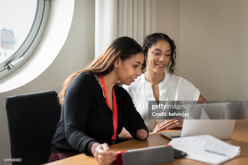 Young black woman with a limb difference, working with colleague in an office