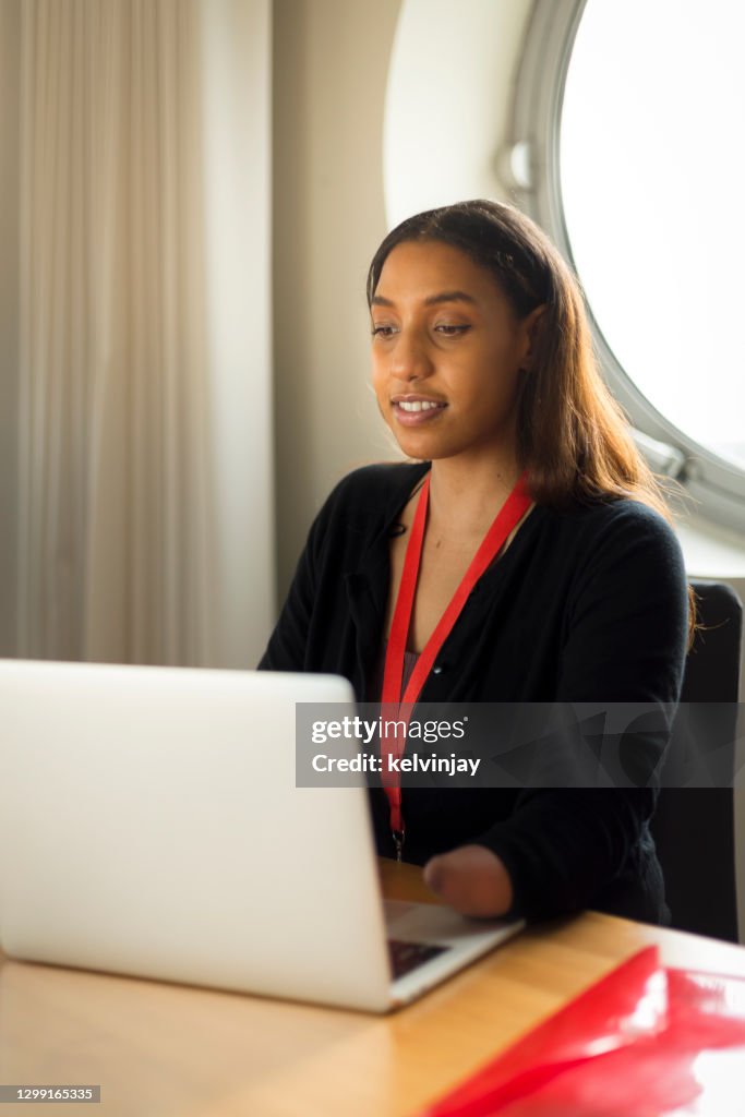 Young black woman with a limb difference, using a laptop computer in an office.