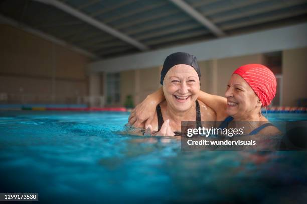 two senior women embracing together in swimming indoor pool - senior swimmers stock pictures, royalty-free photos & images