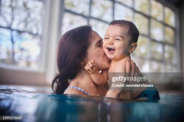 mother kissing happy baby swimming in indoor pool - baby swimmer stock pictures, royalty-free photos & images