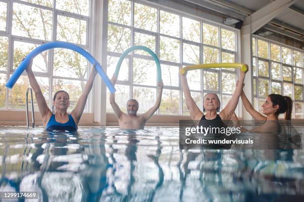 senioren heben poolnudeln im aerobic-klassenpool mit trainer - aquarobics stock-fotos und bilder