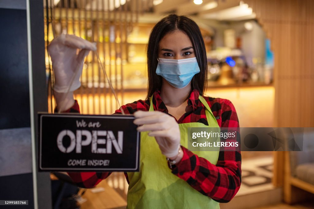 Woman with a face mask holding an "open" sign in her hands