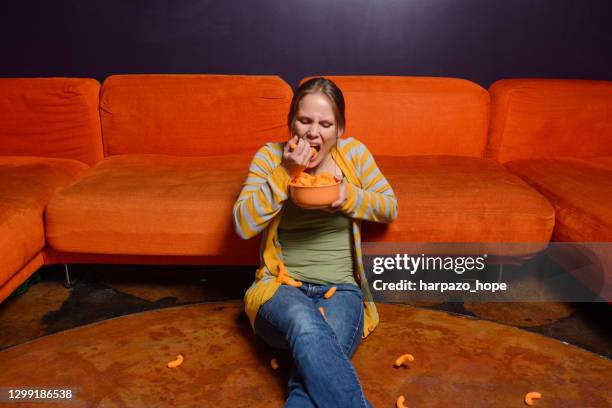 woman sitting on the floor eating cheese puffs by the handful. - bulimie stock pictures, royalty-free photos & images