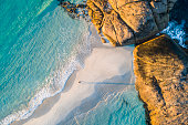 Coastline aerial photograph of aquamarine ocean and man walking along white sandbar beach