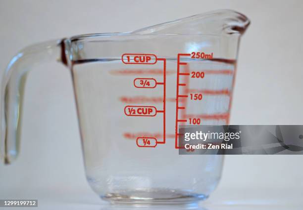 one cup of clear water in a measuring glass cup with handle on white background - mass unit of measurement stock-fotos und bilder