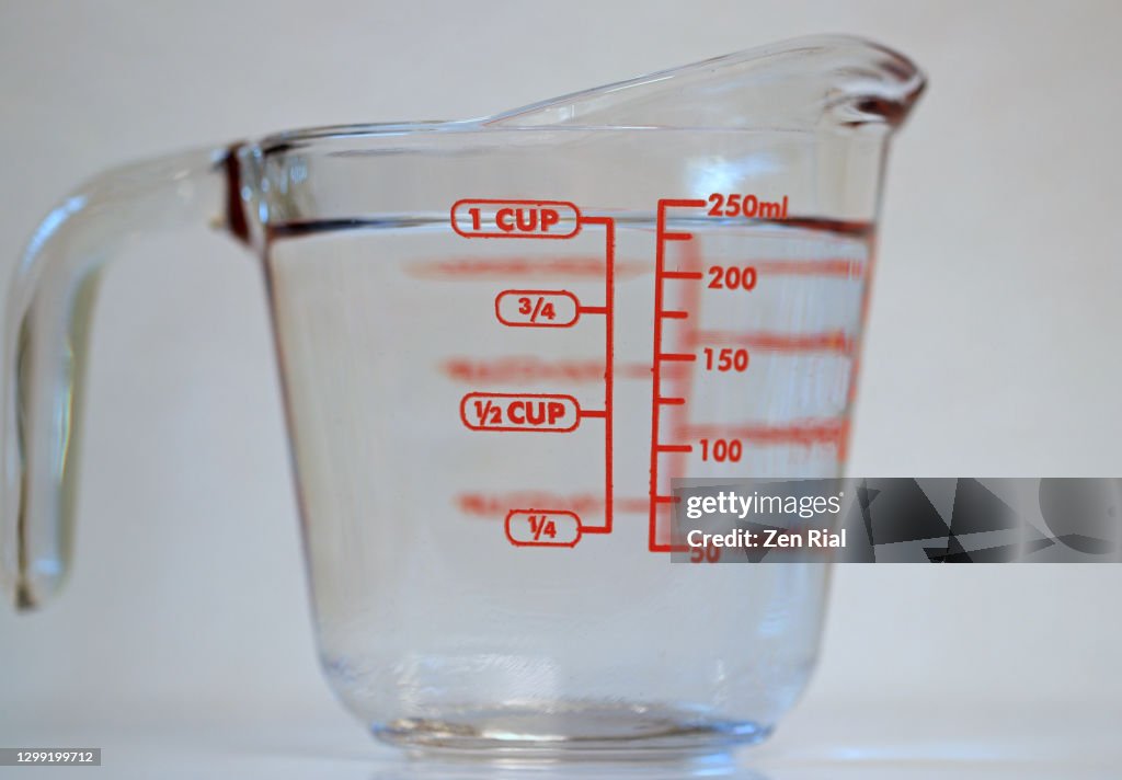 One cup of clear water in a measuring glass cup with handle on white background