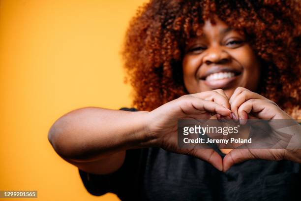 studio portret van een gelukkige, mooie, glimlachende jonge afrikaanse amerikaanse vrouw die een vorm van het hart met haar handen maakt om liefde, verzoening, of dankbaarheid te tonen - anti racisme stockfoto's en -beelden