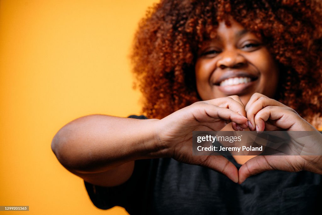 Studio Portrait of a Happy, Beautiful, Smiling Young African American Woman Making a Heart Shape with Her Hands to Show Love, Reconciliation, or Gratitude