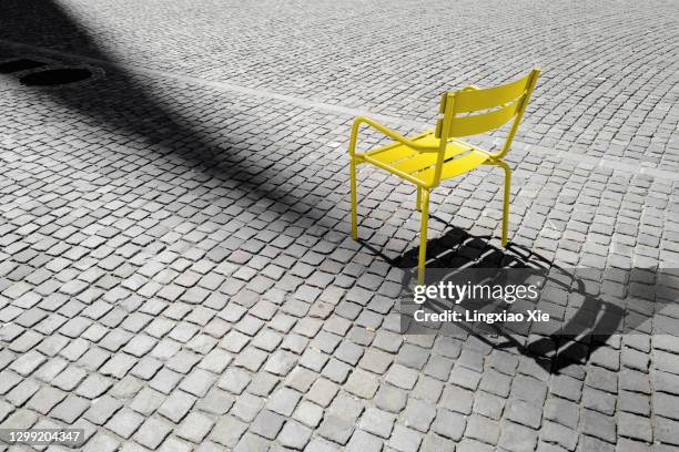 color of the year 2021 - illuminating and ultimate gray: yellow metal chair on cobblestone of town square, zurich, switzerland - zürich stock-fotos und bilder