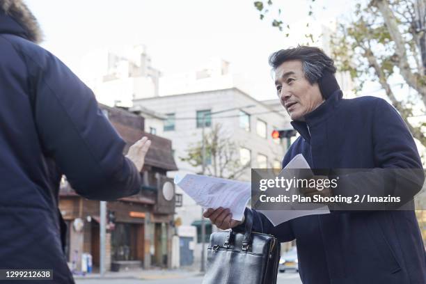 unemployeed middle-aged man giving flyers to people in winter - flyers business people stockfoto's en -beelden