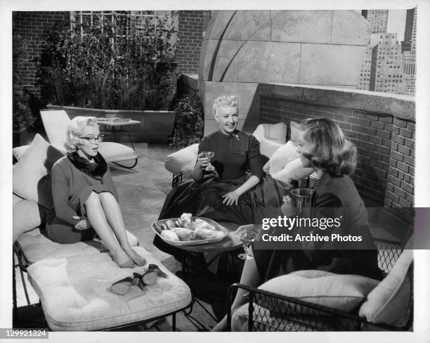 Marilyn Monroe, Betty Grable, and Lauren Bacall having conversation on patio in a scene from the film 'How To Marry A Millionaire', 1953.