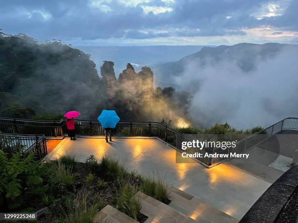 three sisters with clouds in valley, tourists with umbrellas looking at view at night - blue mountains australië stockfoto's en -beelden