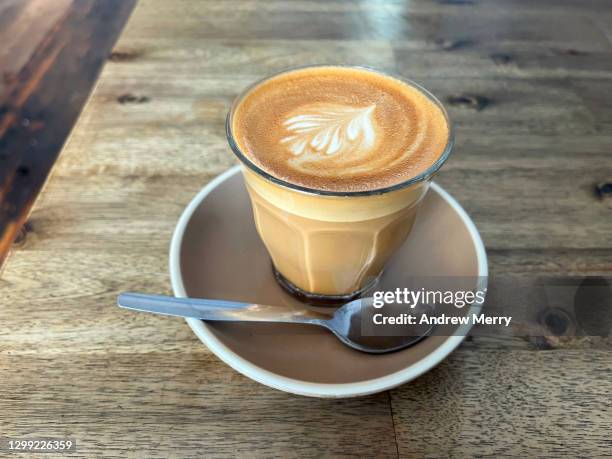 freshly made milk coffee, latte in glass cup, saucer on wooden table, coffee shop - crema stock pictures, royalty-free photos & images