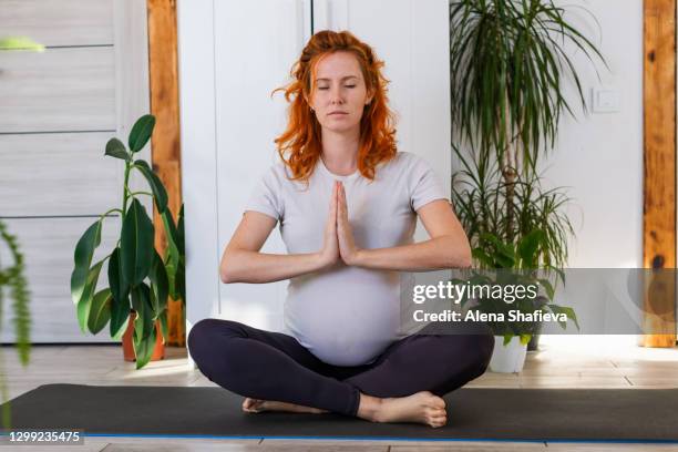 happy pregnant woman practices yoga while staying at home online on a laptop. meditation, yoga postures. healthy lifestyle concept. conscious life, distance learning. - schneidersitz stock-fotos und bilder