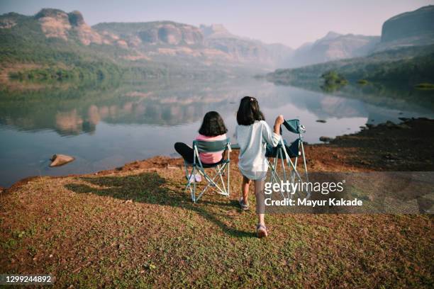Girl carrying a outdoor chair to sit with her sister near a beautiful lakelake
