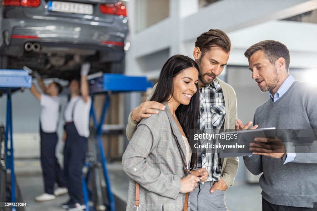 Mid adult manager and young couple using touchpad in auto repair shop.
