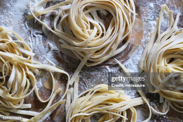 immagine ravvicinata dell'impasto di pasta al nido di tagliatelle fatta in casa spolverata nella farina e lasciata asciugare su tagliere di legno infarinato, cucina italiana vista elevata - tagliatelle foto e immagini stock