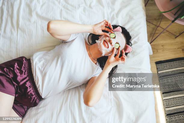 girl in pajamas on the bed in a cosmetic face mask with cucumbers on her eyes. - funny mask stock-fotos und bilder