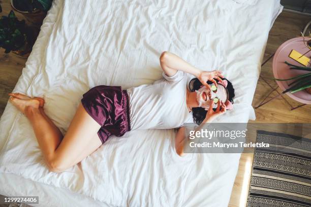 girl in pajamas on the bed in a cosmetic face mask with cucumbers on her eyes. - feierliche veranstaltung stock-fotos und bilder
