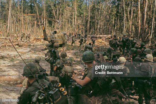 Members of the United States 1st Cavalry look on as a Bell UH-1 Iroquois lands in a clearing bringing reinforcements for their search for Viet Cong...