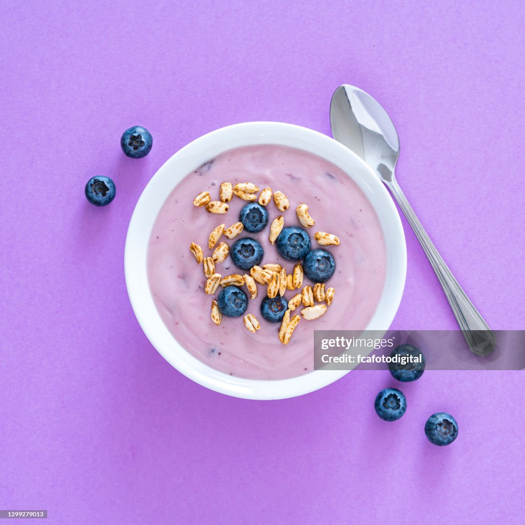 Yogurt with berries and cereal on purple colored background. Overhead view