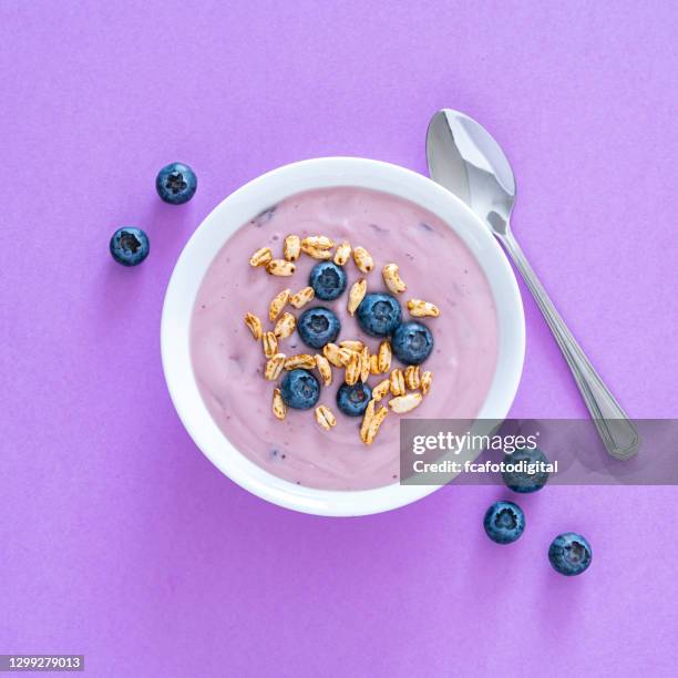 yogurt with berries and cereal on purple colored background. overhead view - tigela imagens e fotografias de stock