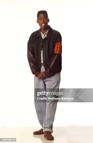 Portrait of American actor and comedian Chris Rock, dressed in a jacket with a laarge letter 'R' on the sleeve as he poses in front of a white...