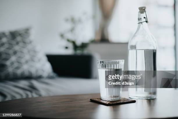a glass of water served on the coffee table next to a bottle of water in the living room at home. healthy lifestyle and stay hydrated - enjoying coffee cafe morning light stock-fotos und bilder
