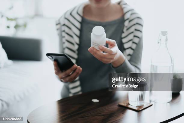 close up of young asian woman holding a pill bottle, consulting to her family doctor online in a virtual appointment over the smartphone at home - medikamente stock-fotos und bilder
