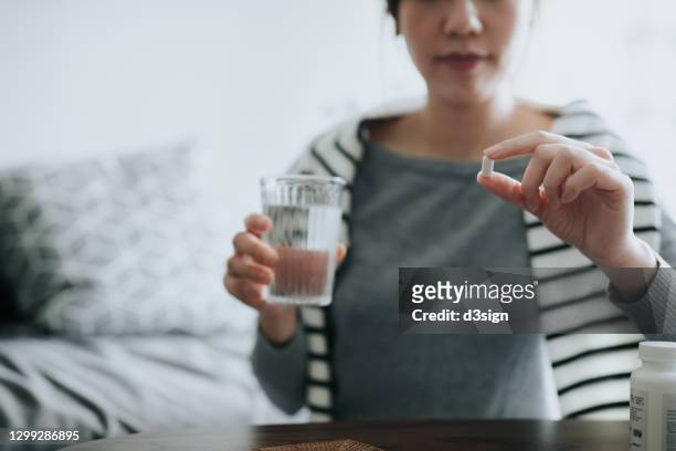 young asian woman taking medicines with a glass of water at home, with a pill bottle by the side. medicine, healthcare and people concept - diabetes pills stock pictures, royalty-free photos & images