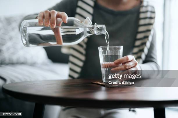 close up of young asian woman pouring water from bottle into the glass on a coffee table at home. healthy lifestyle and stay hydrated - bus sign photos et images de collection