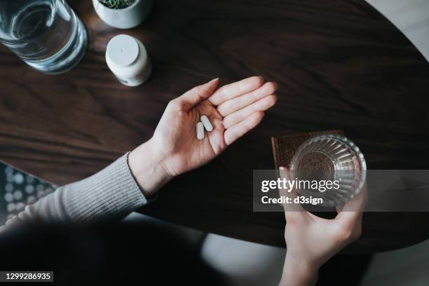 overhead view of young woman holding a glass of water, taking medicines at home. medicine, healthcare and people concept - contraceptive pill stock pictures, royalty-free photos & images