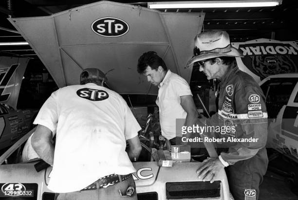 Richard Petty, driver of the STP Pontiac, watches his crew members work on his race car in the Daytona International Speedway garage prior to the...