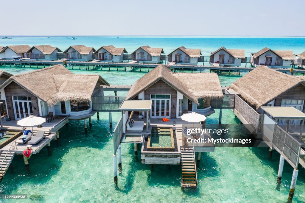 Drone view of luxury bungalows in the Maldives, man on the stairs arms outstretched