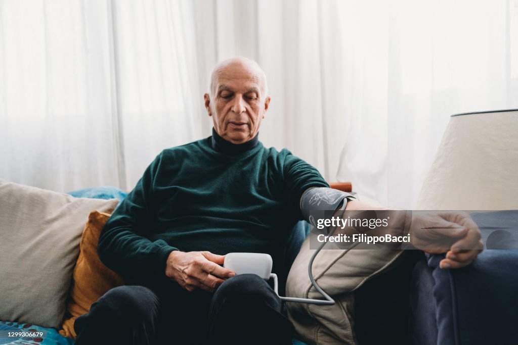 Senior man checking his own blood pressure at home on the sofa