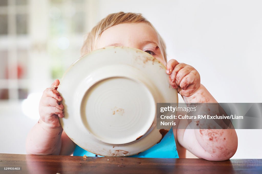 Messy toddler boy licking plate