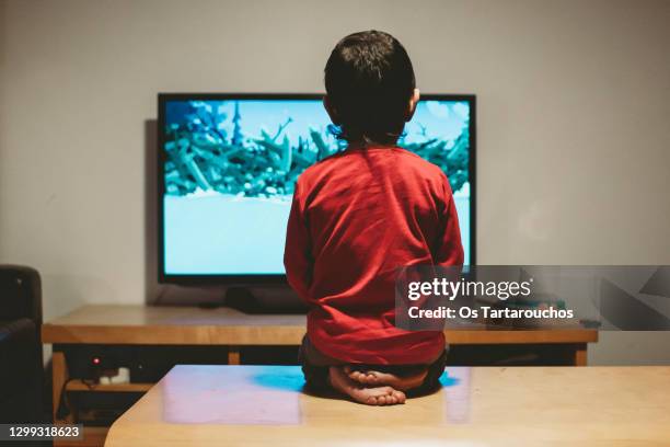 rear view of a boy sitting on the coffee table looking at the tv - boy at television stockfoto's en -beelden