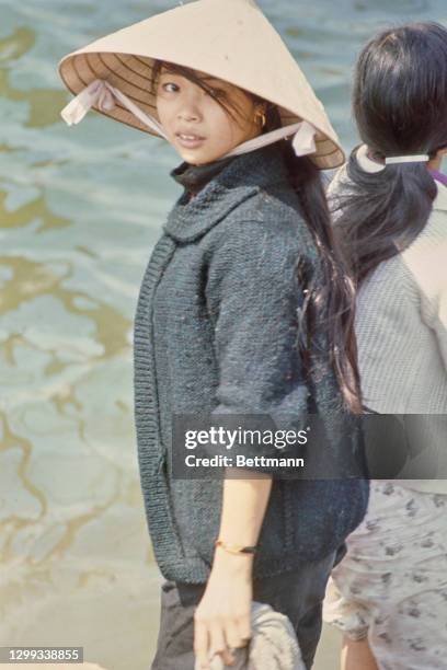 Young Vietnamese woman wearing a traditional non la hat, and a knitted sweater, during the evacuation of Hue, Vietnam, 12th February 1968.