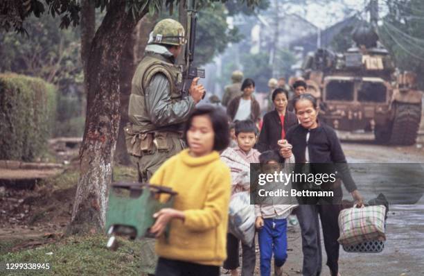 South Vietnamese refugees carrying their belongings under the watchful eye of a military presence overseeing the evacuation of Hue, Vietnam, 13th...