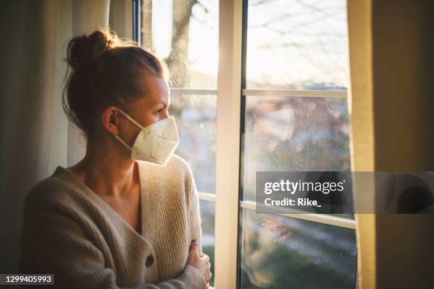 pretty woman in quarantine with mask, looks out the window - covid quarantine stock pictures, royalty-free photos & images