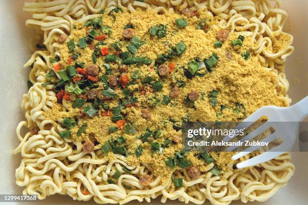 dry, uncooked instant noodles sprinkled with spices, vegetables and herbs, and freeze-dried meat. next to it is a disposable plastic fork. asian chicken noodle soup ramen, textured food background. - ramen noodles fotografías e imágenes de stock