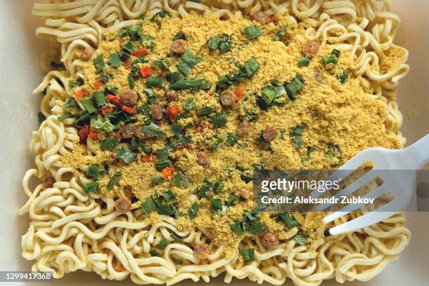 dry, uncooked instant noodles sprinkled with spices, vegetables and herbs, and freeze-dried meat. next to it is a disposable plastic fork. asian chicken noodle soup ramen, textured food background. - dry pasta stock pictures, royalty-free photos & images