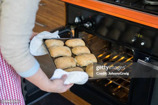 baker removing pan of hot ciabatta rolls from domestic oven - ciabatta stock pictures, royalty-free photos & images