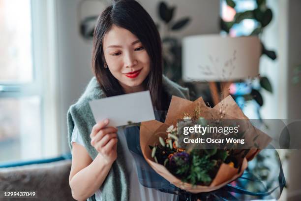 young asian woman reading greeting card attached and holding flower bouquet - san valentino festività pubblica foto e immagini stock
