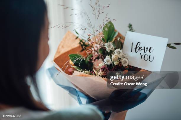 over-the-shoulder view of a unrecognisable woman receiving flower bouquet with greeting card written "i love you" - love you stockfoto's en -beelden