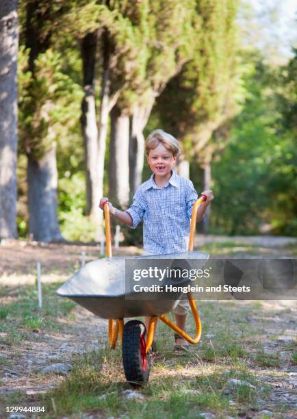 boy pushing wheelbarrow outdoors - kruiwagen stockfoto's en -beelden