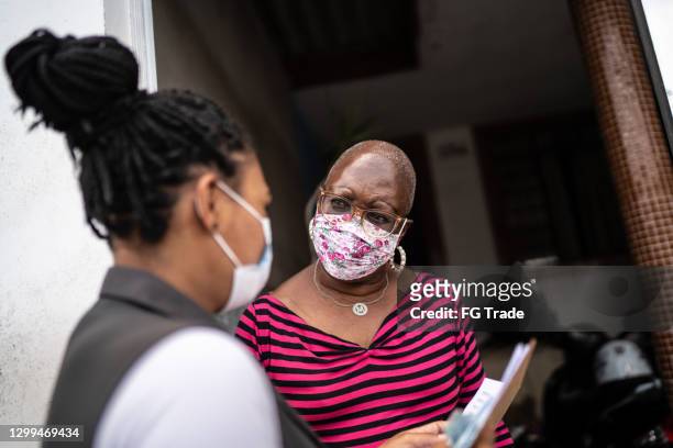 geometra che parla con una donna anziana sulla porta - indossando la maschera facciale - petizione foto e immagini stock
